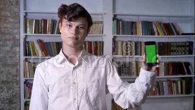 布鲁内特曼正在展示智能手机的绿色屏幕，在镜头下观看，交流概念，背景图书馆